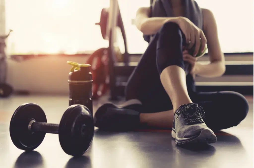 Dumbbells on a gym floor beside a person resting between sets