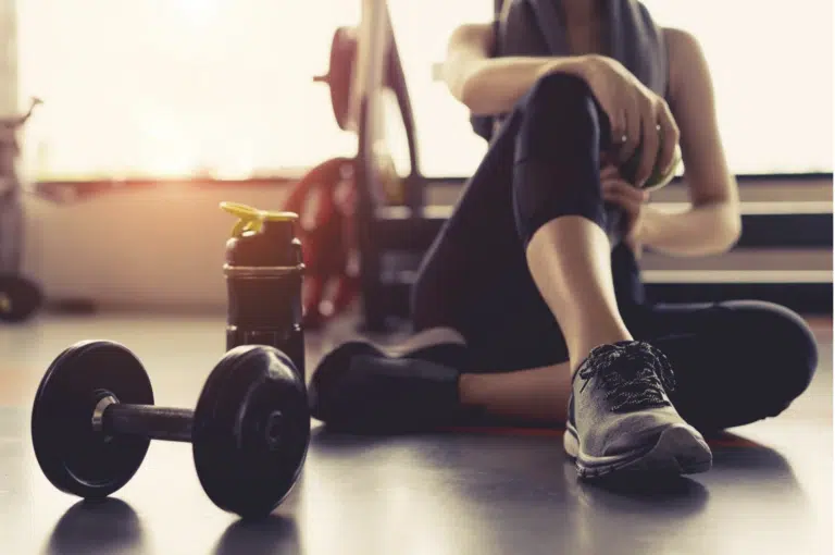Dumbbells on a gym floor beside a person resting between sets