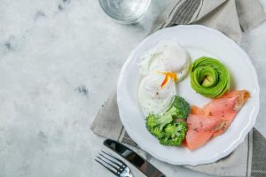 A photo of typical meal on the keto diet: poached eggs, raw broccoli, avocado slices, and smoked salmon.